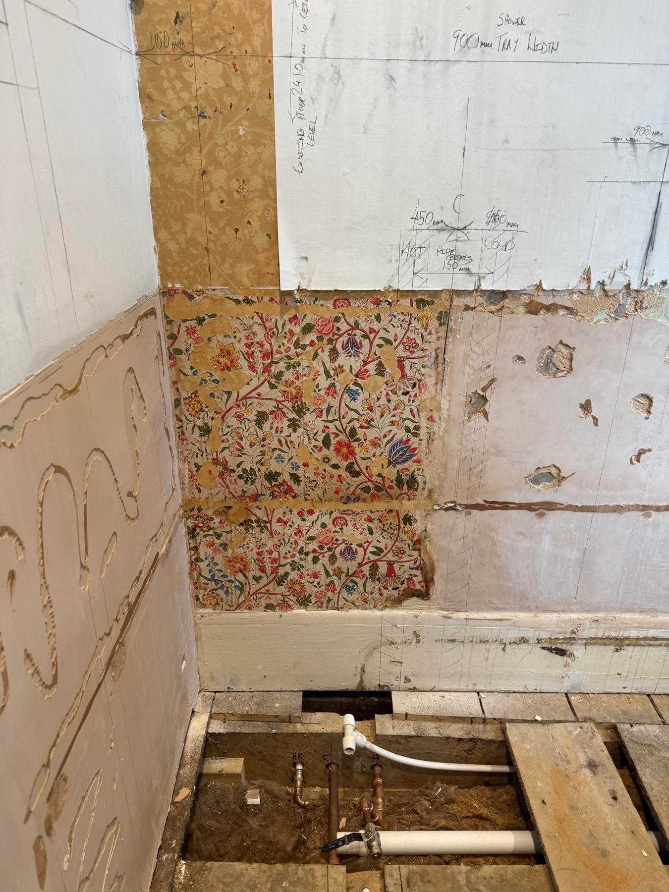Bathroom stripped back to bare walls with old wallpaper exposed before the refit