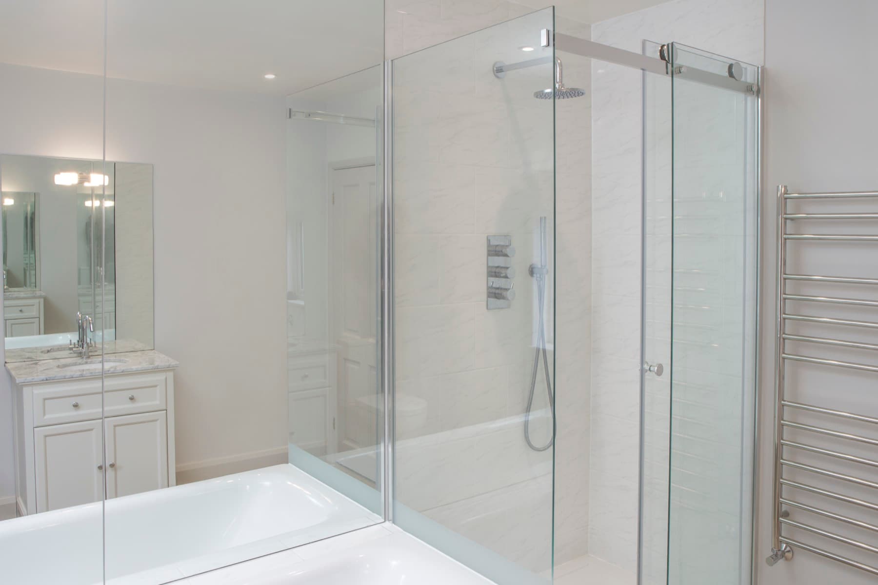 Frameless glass shower enclosure with a fixed rainfall head and heated towel rail