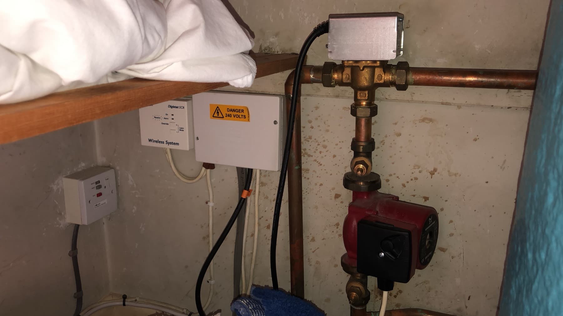 Three-port mid-position valve above a red circulating pump in an airing cupboard, with a wiring centre on the wall