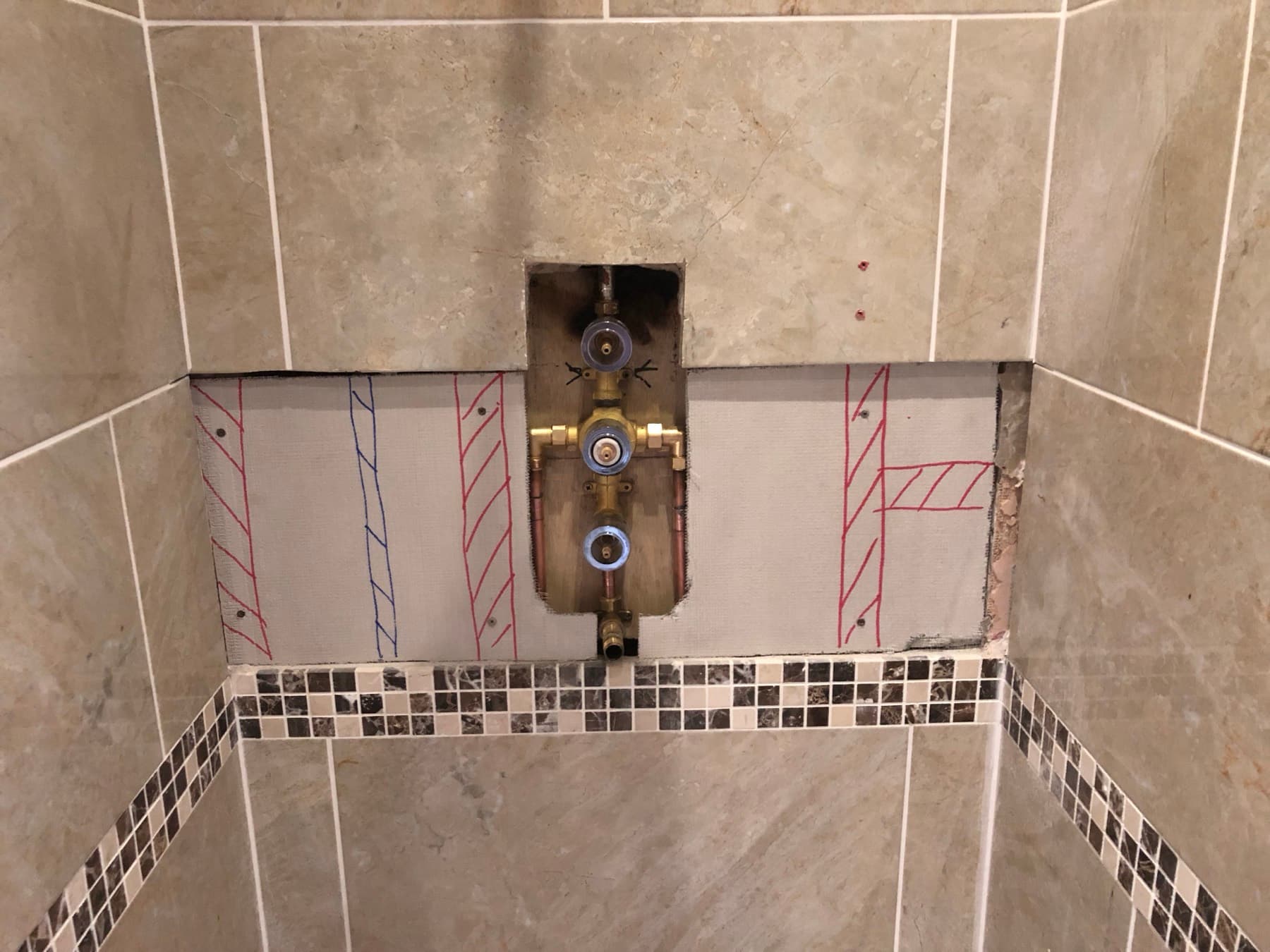 Brass concealed shower valve body exposed in a cut-out in a tiled wall, with pipe runs marked on the board