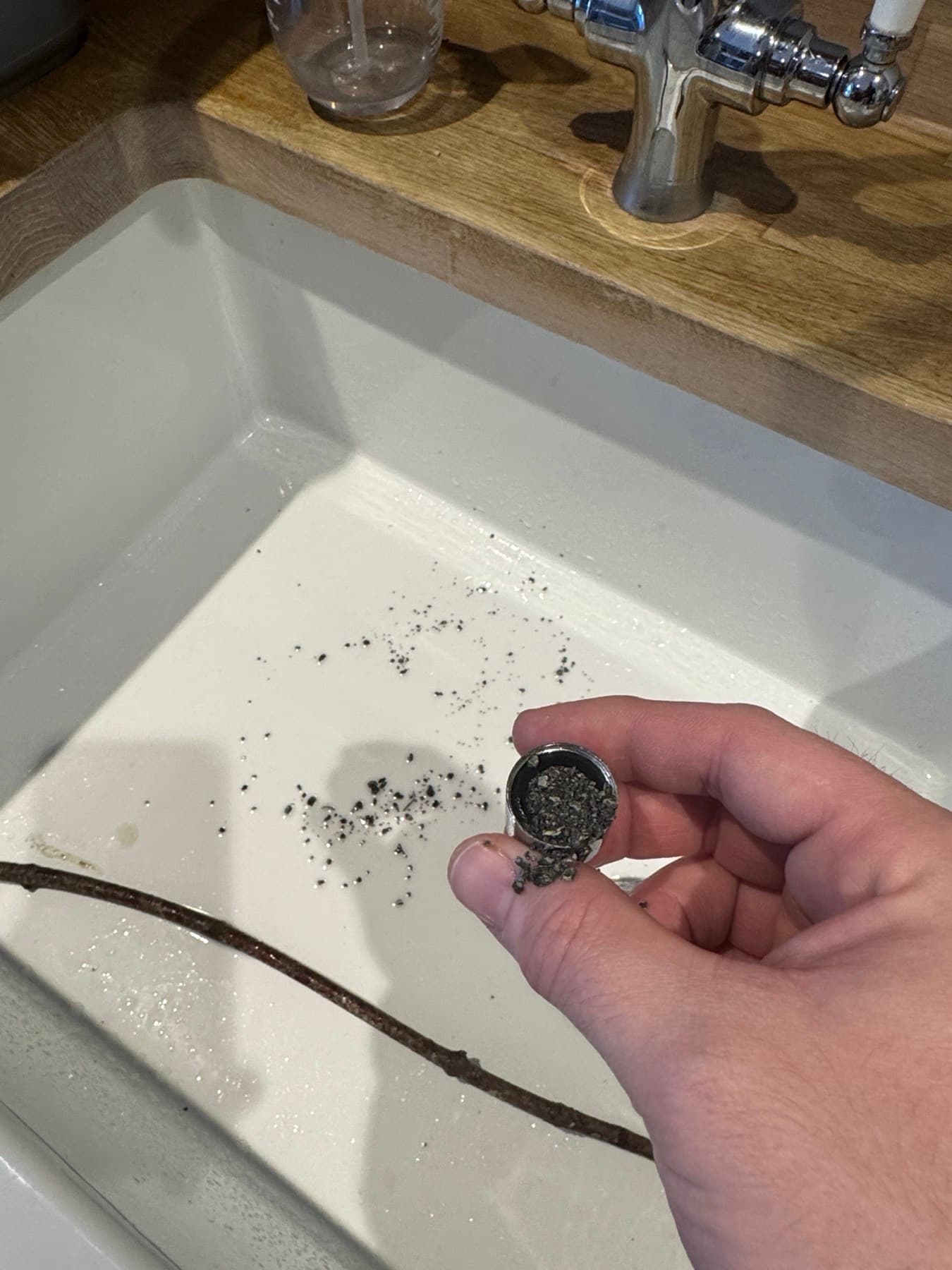Tap spout aerator filter held over a Belfast sink, packed with black grit from the cold main