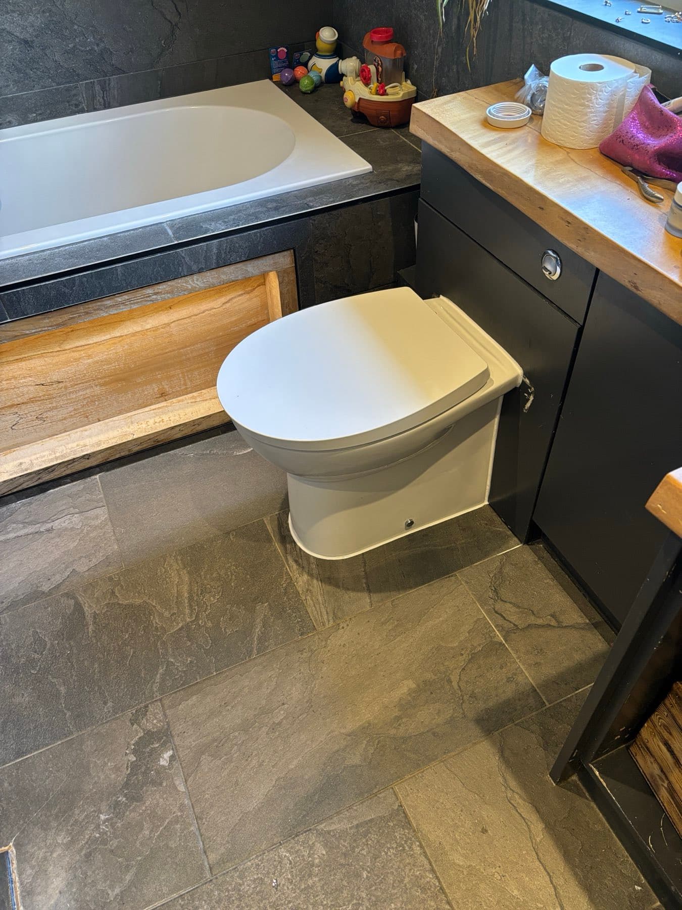 Back-to-wall toilet fitted in a slate-tiled bathroom by Rosebourne Plumbing