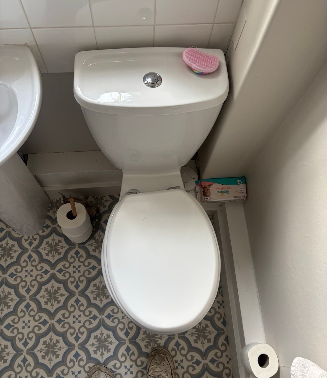 Close-coupled toilet fitted in a small cloakroom with a patterned tiled floor