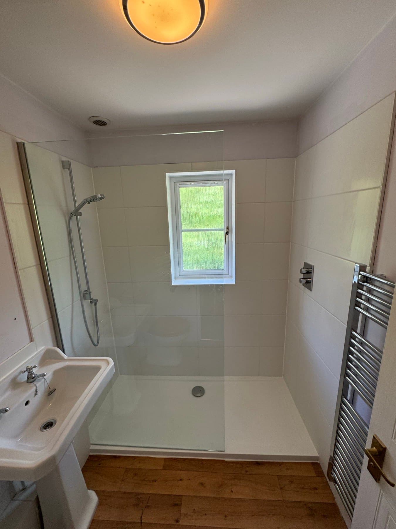 Walk-in shower with a low tray, fixed glass screen, thermostatic shower and chrome towel rail, converted from a bath by Rosebourne Plumbing
