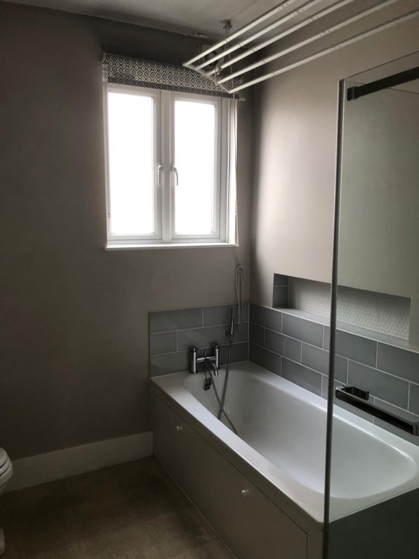 Reinstated bathroom with a grey bath, glass screen and white subway tiles, fitted by Rosebourne Plumbing