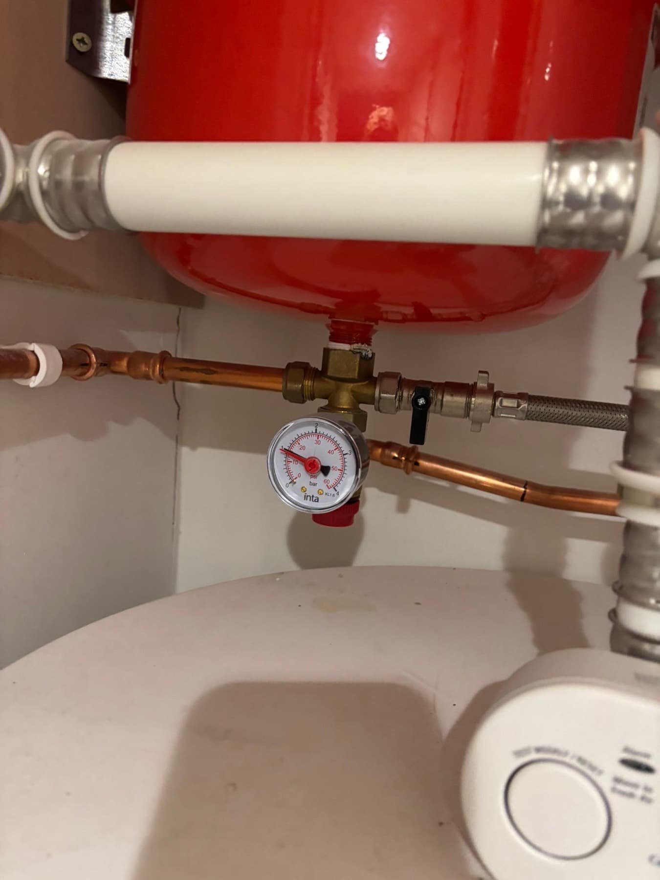 Pressure gauge on the pipework under a red expansion vessel above a cylinder