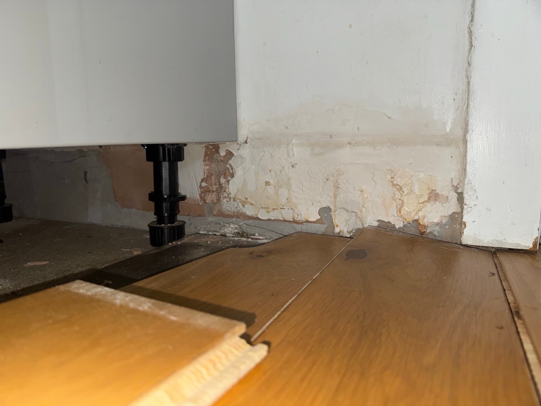 Damp staining on a wall uncovered behind a kickboard after a slow leak
