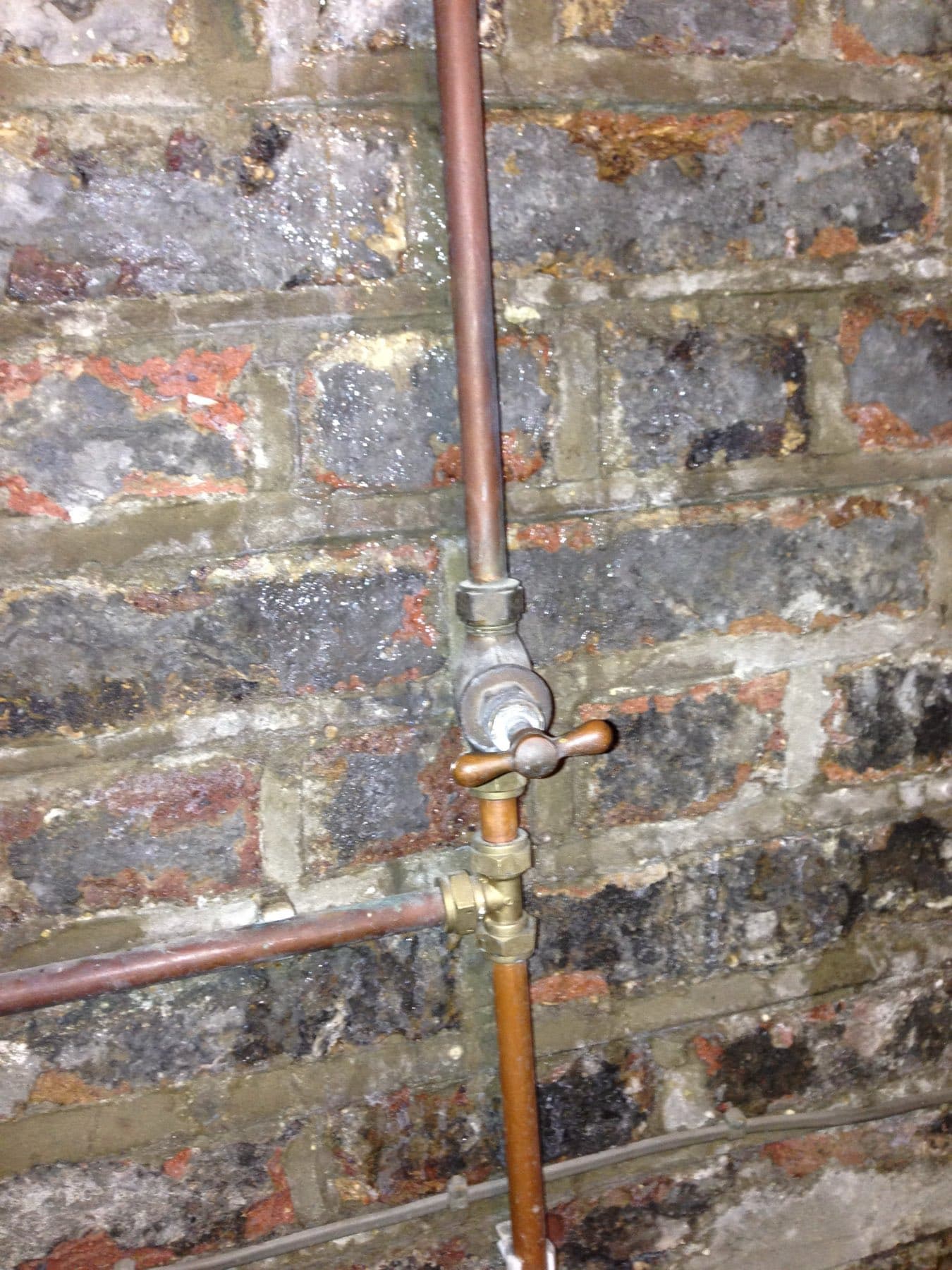 Brass stopcock on a copper rising main against a bare brick wall